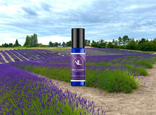 Vibe Lavender essential oil rollerball bottle displayed in the center of a blooming lavender field under a cloudy sky, showcasing the product’s natural origin and calming botanical environment.