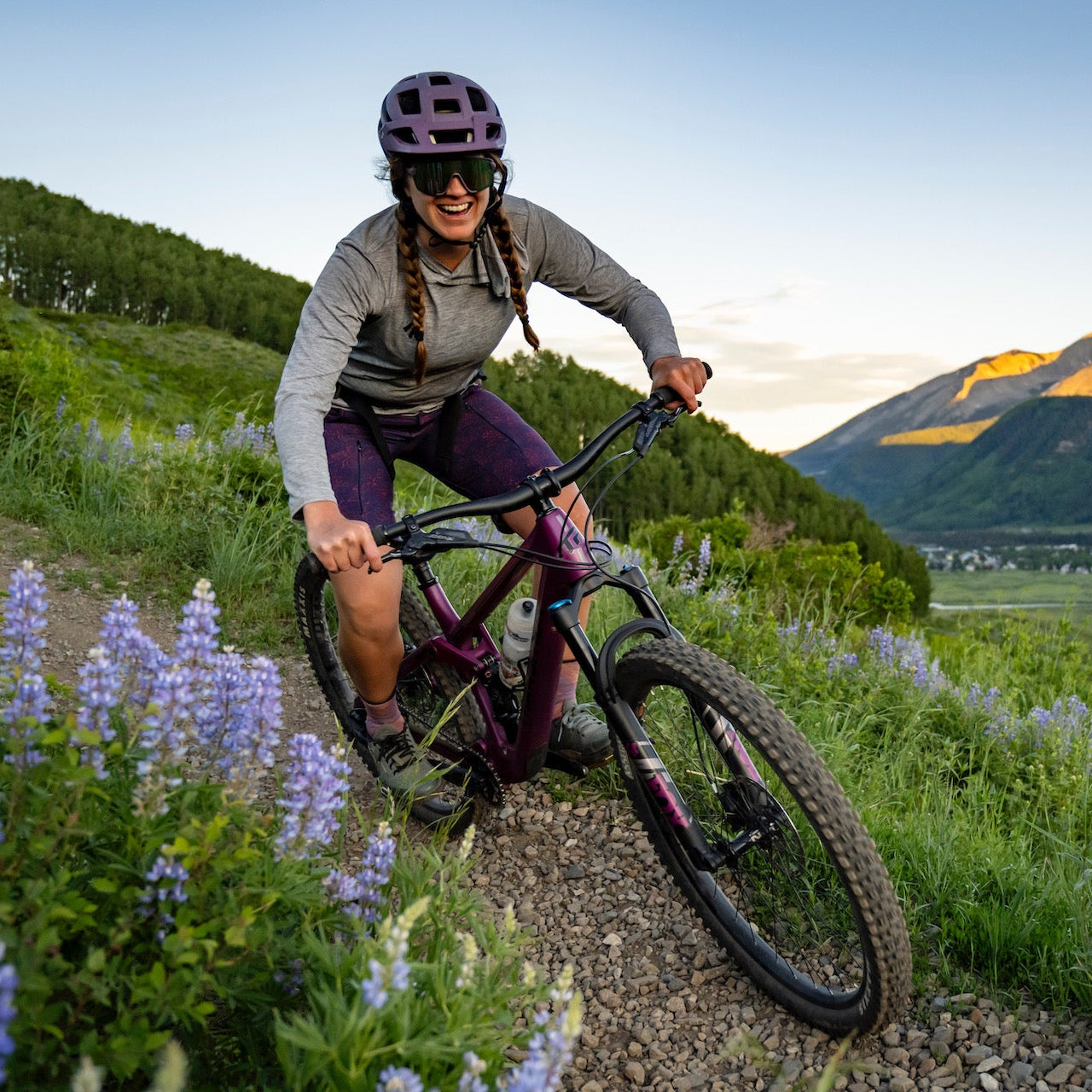 Person mountain biking on a trail with mountains and flowers in the background