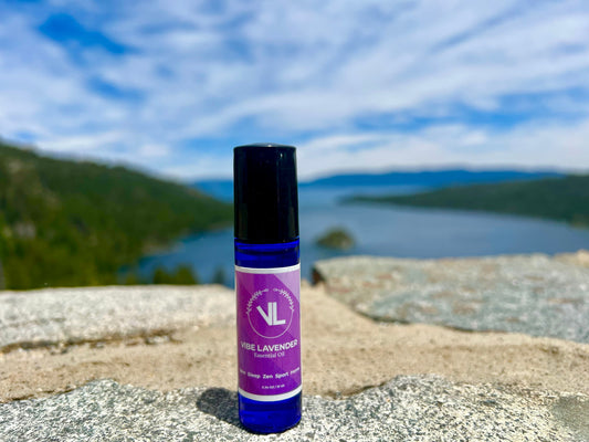 Vibe Lavender essential oil rollerball bottle placed on a stone surface with a stunning Lake Tahoe mountain and lake view in the background, symbolizing natural wellness and daily self-care.